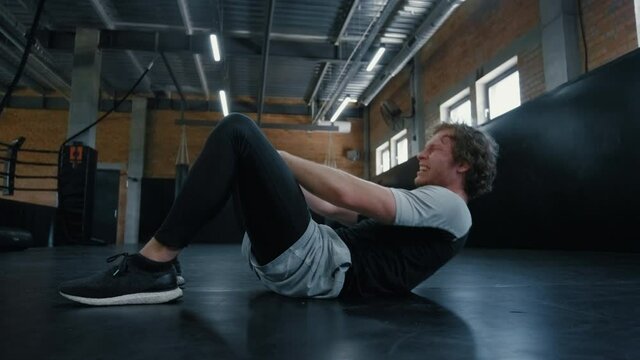 Young kickboxer doing crunches in sport club. Sportsman working on abc at gym