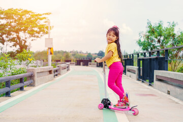 Little child girl to ride scooter in outdoor sports ground on sunny summer day. Active leisure and outdoor sport for children.