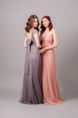 Two beautiful bridesmaids in long fashionable chiffon dresses posing in the studio. Full length portrait.