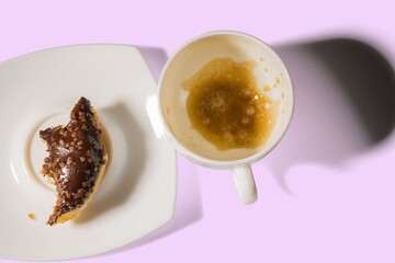 View of empty cup with rest of coffee and piece of chocolate  donut isolated on pink background. Food and drink concept.