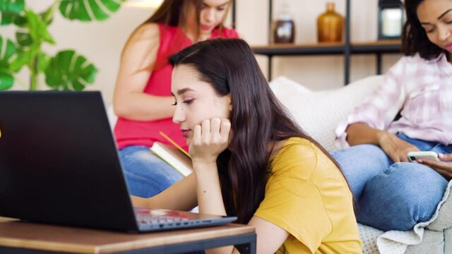 Arabian student sitting on floor and receiving good news on laptop, her multiracial friends feeling happy for her and giving high five. Roommates sharing great moments together