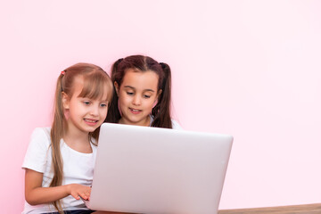 Two little girls sitting in front of a laptop and laughing, close-up, positive emotions, entertainment on the Internet for children