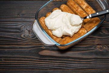 tiramisu dessert cooking - Traditional Italian Savoiardi ladyfingers Biscuits and cream in glass baking dish on wooden background