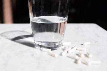 White pills tablets on a white marble table isolated glass of water bright light health