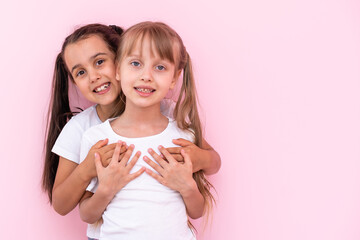 Two little girls hugging each other. Isolated on on a pink background