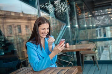 Excited happy Indian girl celebrating online win, holding phone, looking at camera sitting at home...
