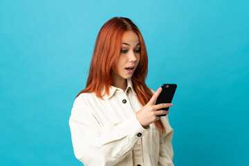 Teenager Russian girl isolated on blue background sending a message or email with the mobile