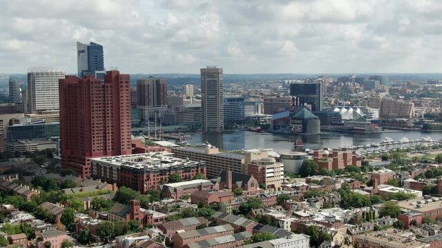 Rising aerial establishing shot as clipper ship sailboat enters Inner Harbor in Baltimore Maryland USA on summer day, city urban skyline under beautiful clouds, neighborhood ocmmunity houses below