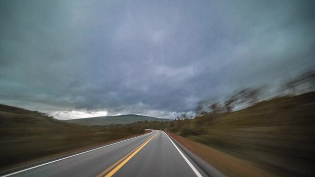 A drive on the E39 in Northern Norway. Narrow two lane freeway leading through the tundra. Moss, lichen and grass colored in orange and brown cover the landscape. Gray clouds hanging above.