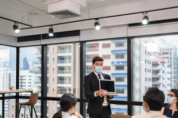 Fototapeta premium Businessman wearing face mask with presentation of business plan on laptop. Corporate business meeting in modern office