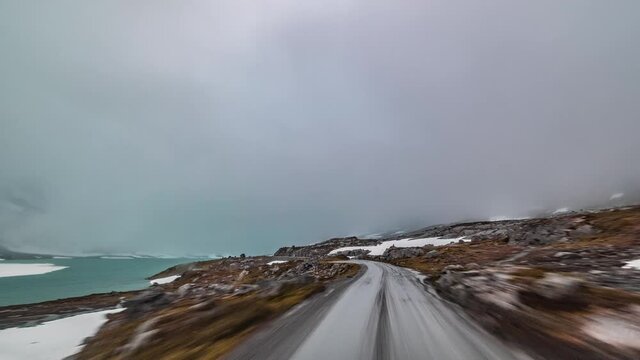 A drive on the County Road 258 towards Stryn, Norway. Thick white-gray clouds hanging above.Ice cold lakes with bright turquoise water stretch along the road. Snow starts to fall.
