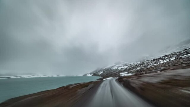 A drive on the mountainous plateau on country road 258 towards Stryn, Norway. Thick white-gray clouds hanging above. The harsh tundra landscape is on both sides of the road. Rain starts to fall.