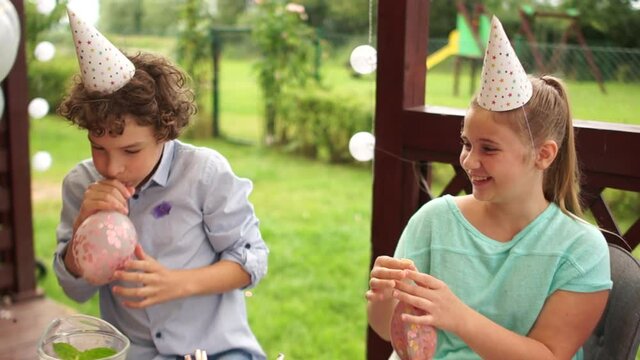 Happy childhood. Teenagers in birthday hats oy and girl at the birthday party have fun stuffing big balloons with sparkles inside