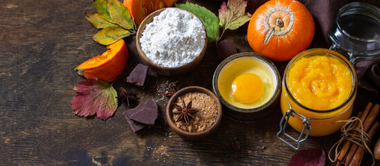 Obraz na płótnie Canvas Seasonal food background - ingredients for autumn baking (pumpkin puree, eggs, flour, chocolate, sugar and spices) on a wooden table. Banner.