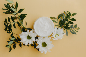 Fototapeta na wymiar Cosmetic cream with flowers on yellow background.