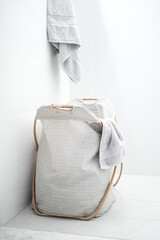 A cloth fabric dirty washing bag basket in a modern simple white bright bathroom lit by natural...