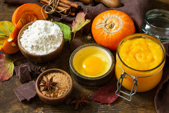 Seasonal food background - ingredients for autumn baking (pumpkin puree, eggs, flour, chocolate, sugar and spices) on a wooden table.