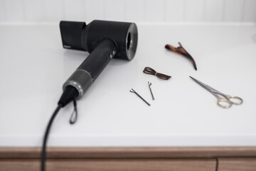 Modern black stylish hair dryer on a white stone vanity top with simple flowers in a vase