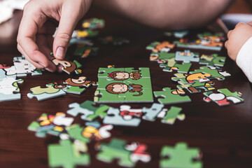 Hands of a little child and parent plying jigsaw puzzle game on a table