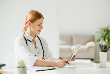 Female doctor working at office desk and smiling, office interior on background