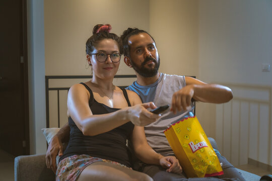 Pareja de novios casados comiendo palomitas viendo television pelicula en casa comodos