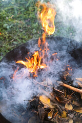 Burning in  barrel of autumn yellow maple leaves with flames and charcoals, the view from above, a lot of smoke, goodbay autumn summer, autumn mood