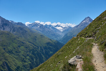 Fototapeta na wymiar Bergweg am Rand eines grünen Berges beim Wandern in den Bergen Alpen Wanderweg