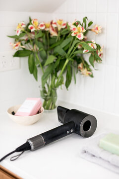 Modern black stylish hair dryer on a white stone vanity top with simple flowers in a vase
