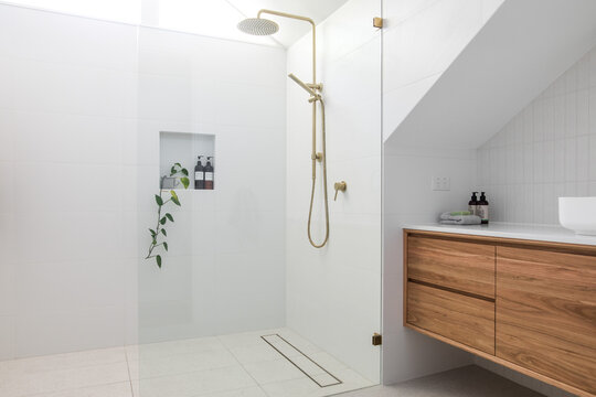 Brushed brass tap mixer on timber vanity with white basin bowl against white tiled wall in a new modern elegant bathroom lit by natural light from a nearby window modern interior house renovation new 