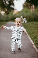 Fototapeta premium boy walking in a beautiful white suit against the background of nature, baby about one year old learning and playing outdoors.