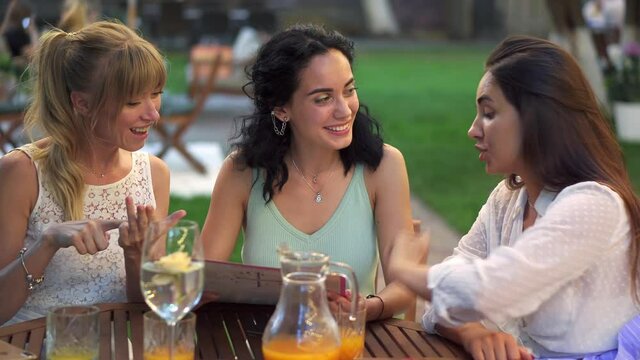 Three beautiful women having fun choosing meal, looking at the menu, laughing and gesturing