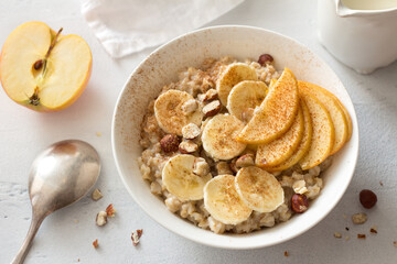 Delicious healthy breakfast. Oatmeal with banana, apple, nuts and cinnamon on a light gray background, top view	