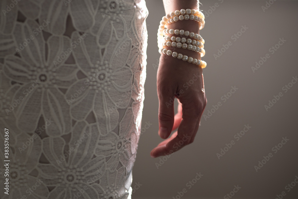 Wall mural a woman wearing a string of pearls as a bracelet a pearl covered purse dressed in a white lace dress