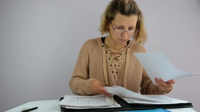 Recorded information. A woman is engaged in office work. A woman works at an offside table. the woman searches for the necessary document, parses and checks the documents.