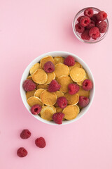 Top view of mini pancakes with raspberries in the white bowl on the pink background.Location vertical.
