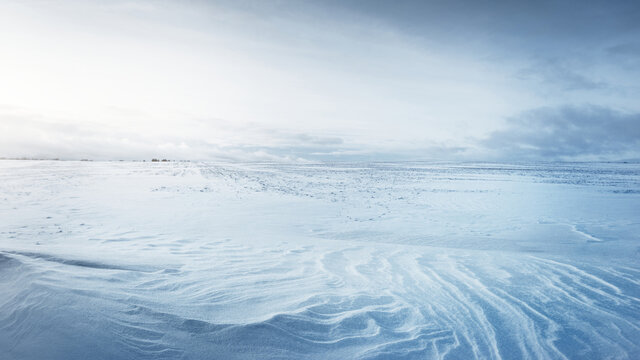 Panoramic view of the snow-covered field after a blizzard at sunset. Human tracks in a fresh snow. Ice desert. Dramatic cloudscape. Global warming theme. Lapland, Finland