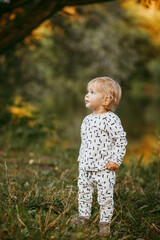 boy walking in a beautiful white suit against the background of nature, baby about one year old learning and playing outdoors.