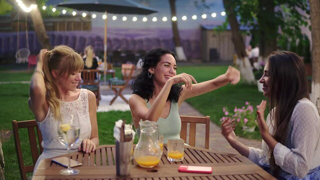 Happy, three attractive women having fun and dancing in the restaurant outdoors in the evening dusk