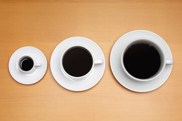 High angle view of three coffee cups arranged according to their sizes on a wooden surface