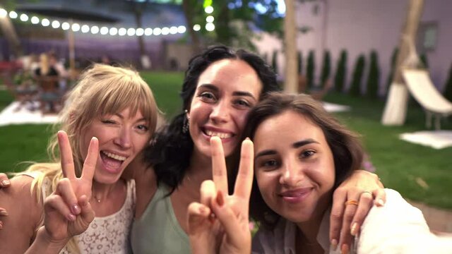 Three attractive women met in veranda cafe outdoors taking selfie photo or video on smartphone