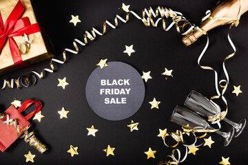 Top view of round with black friday sale lettering near festive decor, bottle of champagne and gift on black background