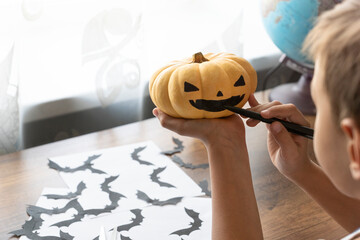 preparations for halloween. close up image of boy dawing scarring face on orange pumpkin.  black...