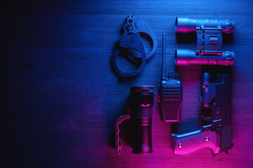 Spy secret service agent desk table concept background. Gun, radio, binoculars, handcuffs and flashlight on the neon background with copy space.