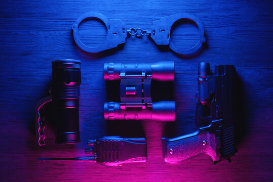 Spy secret service agent desk table concept background. Gun, radio, binoculars, handcuffs and flashlight on the neon background. - Powered by Adobe