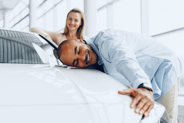 Young couple man and woman hugging their new car in a car shop