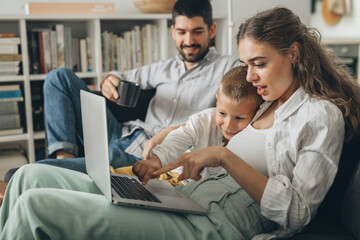 young family sitting on sofa and using laptop computer at home