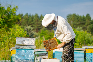 Beekeeper in protective workwear. Hives background at apiary. Man works on the apiaries in spring.