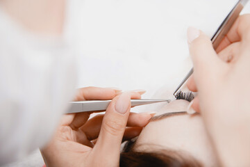 Eyelash extension procedure. Master tweezers fake long lashes beautiful female eyes