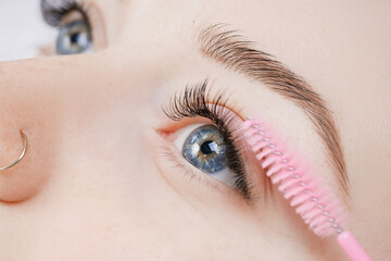 Eyelash extension procedure. Woman master combs lashes fake