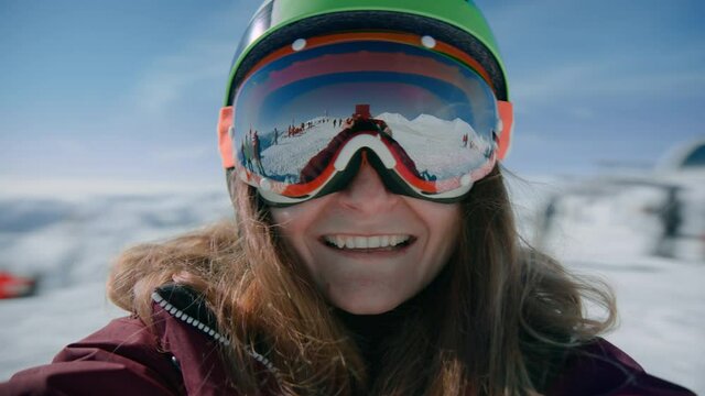 Happy female snowboarder or skier makes selfie and spins around in ski resort. happy vacation portrait or video live coverage for social media.Big reflective goggles and safety helmet. Winter activity